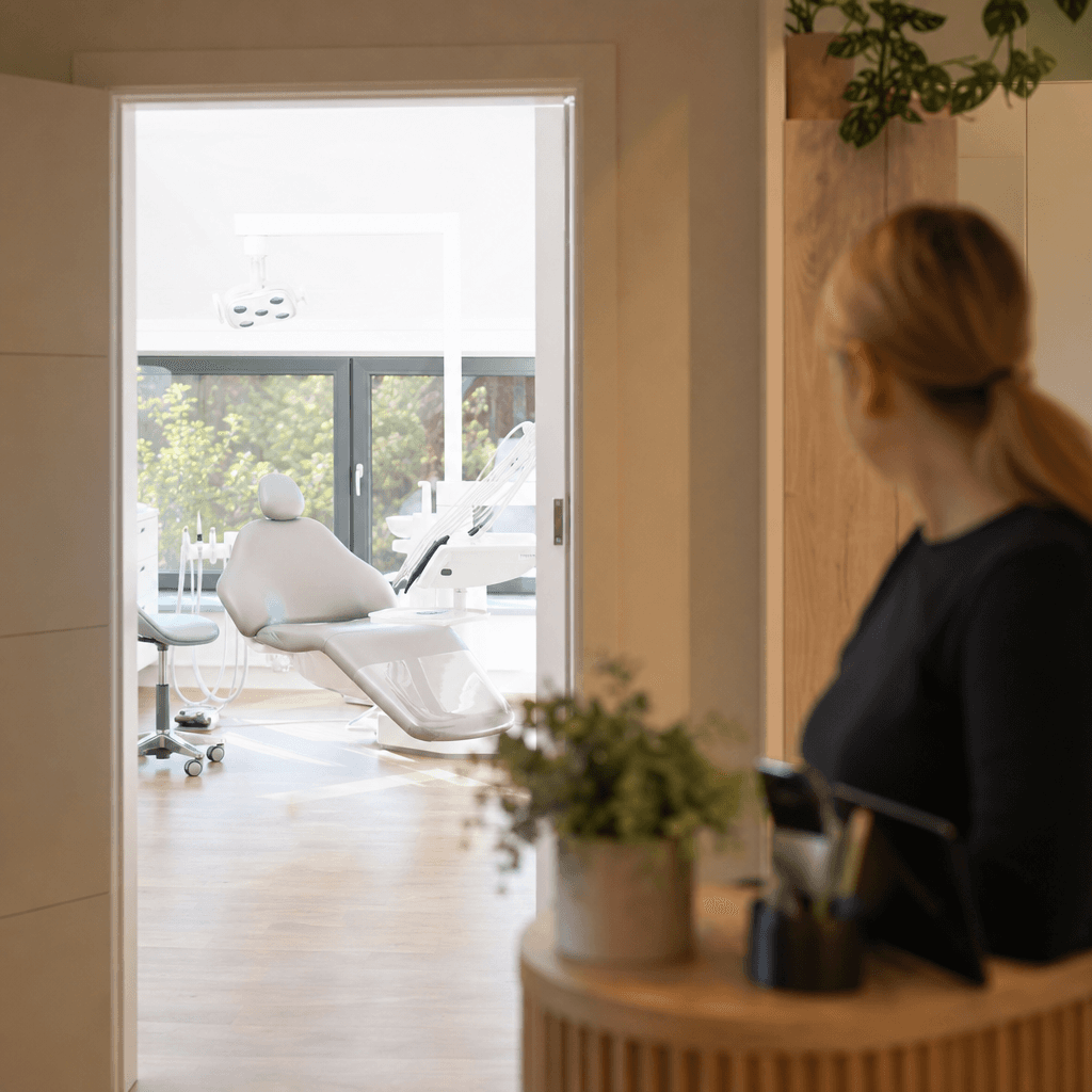 En tom behandlingsstol i ett ljust klinikrum, sedd från receptionen genom en öppen dörr. Symboliserar kostnaden av uteblivna besök.