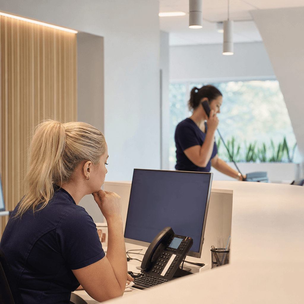 Receptionist på tandklinik som tittar på en datorskärm med inkommande samtal, telefonen ringer i bakgrunden